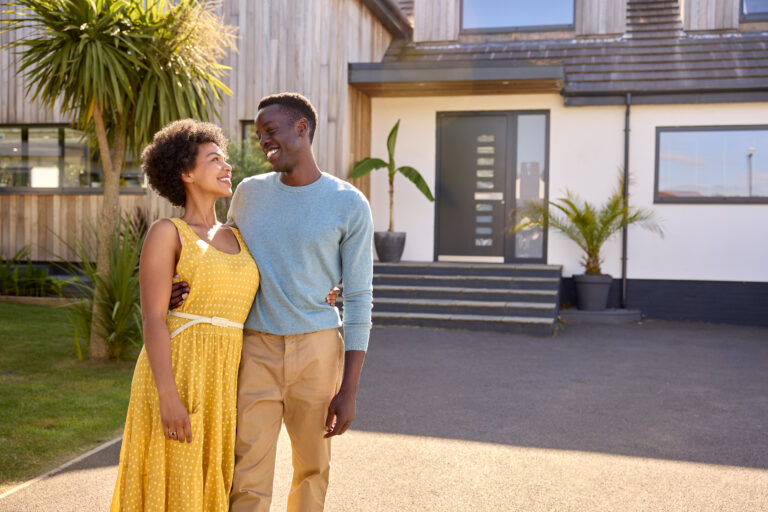A couple smiling in front of their newly purchased dream home after answering the question, What is the difference between jumbo loans and conventional loans?