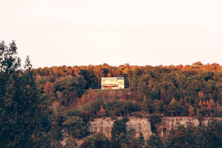 A secluded house sits atop a cliff surrounded by vibrant autumn foliage in Arkansas.