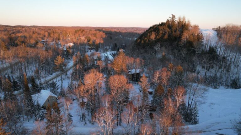 Aerial winter view of snow-covered Huntsville, Ontario, surrounded by forest at sunset.