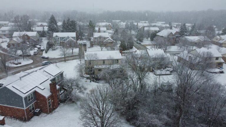 Aerial shot of a suburban neighborhood covered in snow during winter, creating a serene winter landscape.