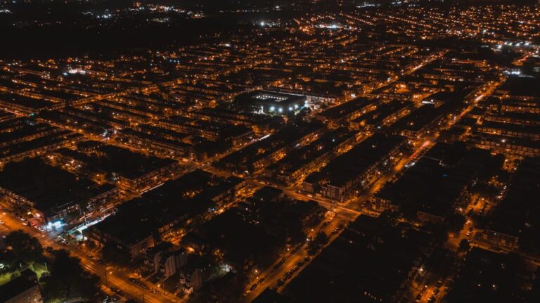 Aerial view of brightly illuminated streets of settlement with silhouettes of buildings at dark night
